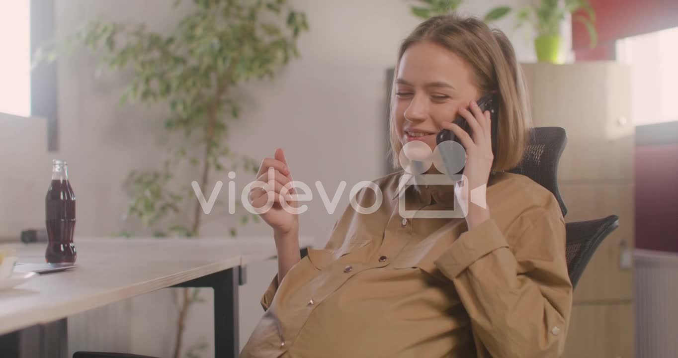 Pregnant Woman Talking On Her Mobile Phone While Sitting At Desk During Office Lunch Break 1