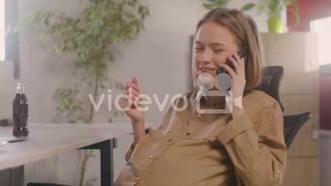 Pregnant Woman Talking On Her Mobile Phone While Sitting At Desk During Office Lunch Break 1