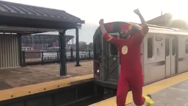 Man in red flash costume running next to subway train