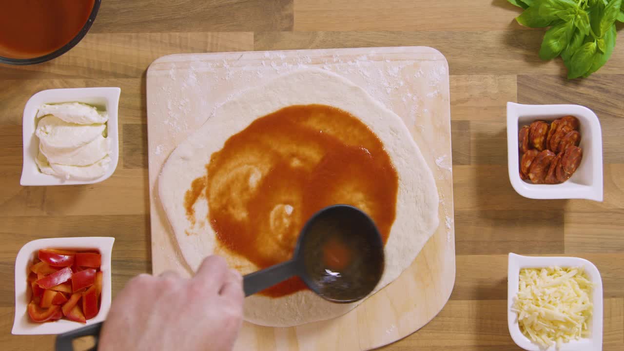 Top View Male Pours and Spreads Sauce on Pizza