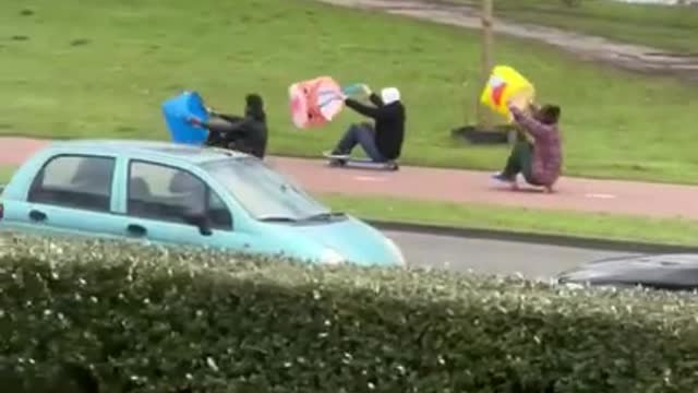 People Sitting on Skateboards Move by Holding Bags Against Wind to Propel Their Rides