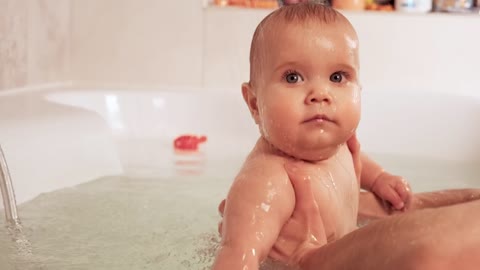 Person holding baby in bathtub with both hands