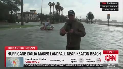 CNN reporter talking about the dangers weather conditions as laughing Floridians paddle past him.