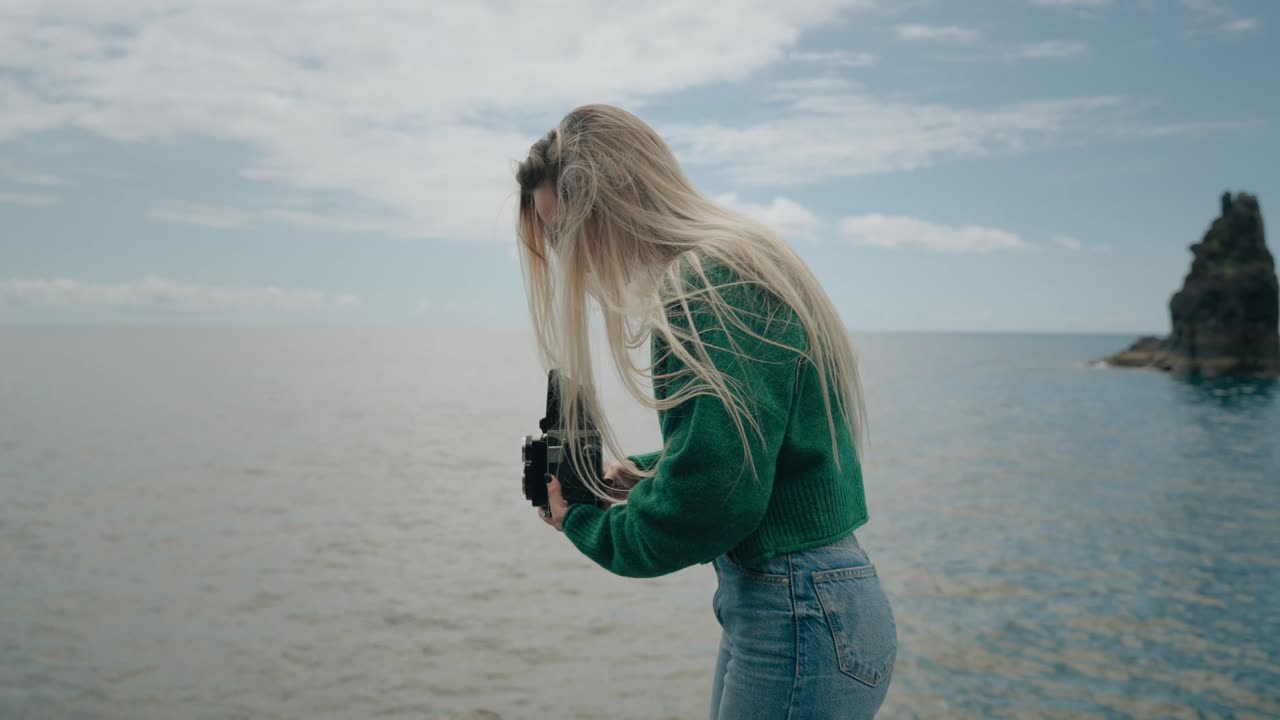 A young woman takes photos of the sea with an old TLR camera