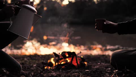 people pouring a warm drink around- a campfire