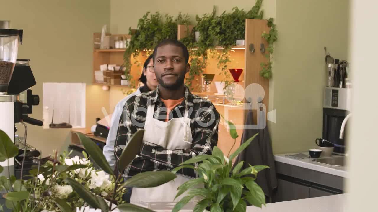 Two Multiethnic Waiters With Crossed Arms Looking At Camera While Standing Behind Counter In A Coffe