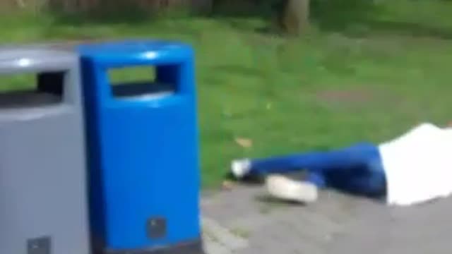 Man in white jumps over blue trash bin and falls forward