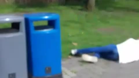 Man in white jumps over blue trash bin and falls forward