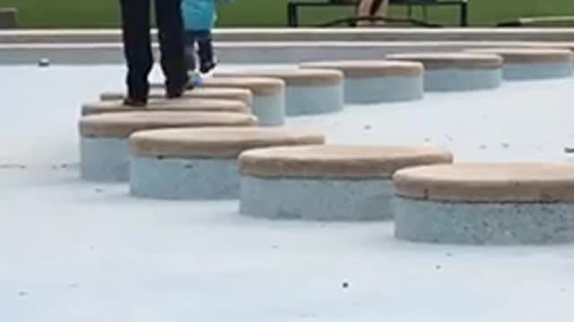 Little boy in light blue sweater walking on circle rocks falls into water