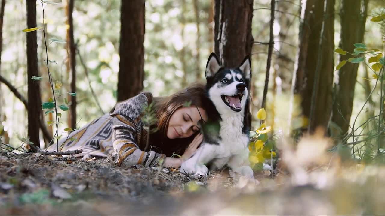 Young natural woman lying on a meadow and hugging her wolf-looking dog