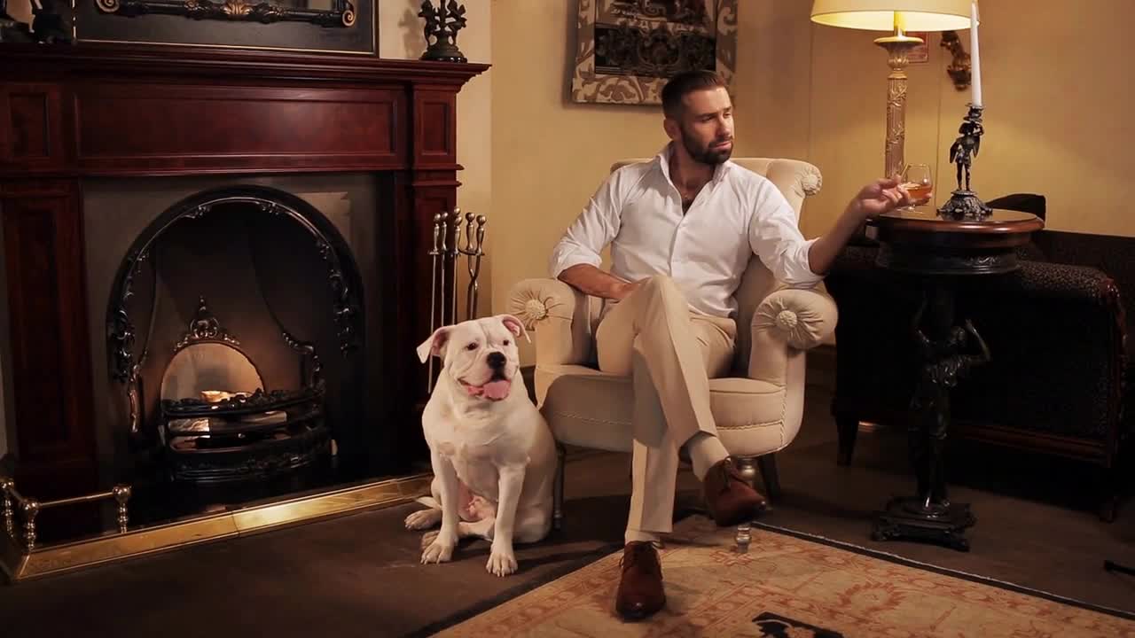 An aristocrat with a dog by the fireplace drinking whiskey