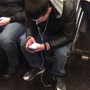 Guy on subway on phone headphones aren't plugged in