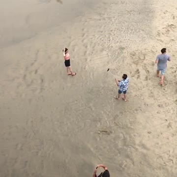 Guy holding selfie stick taking picture of girl at beach