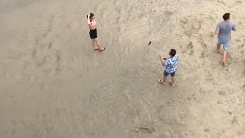 Guy holding selfie stick taking picture of girl at beach