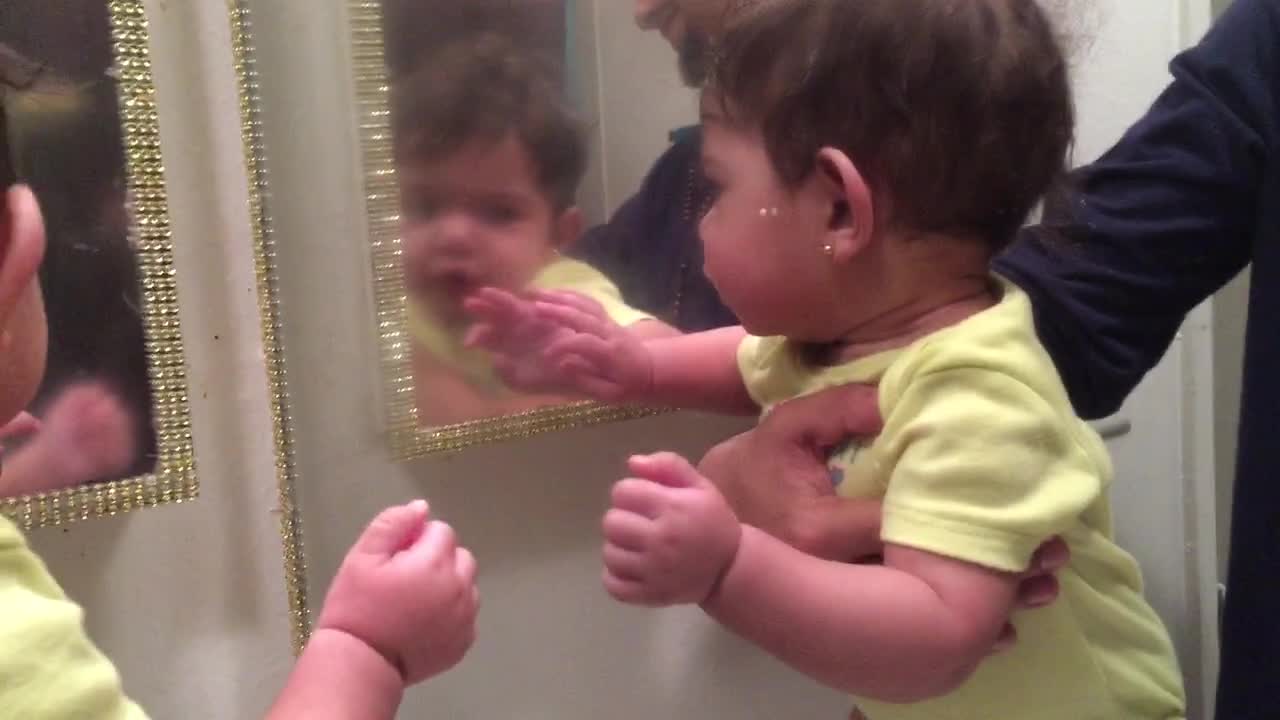 Baby girl attempts to make contact with her mirror reflection