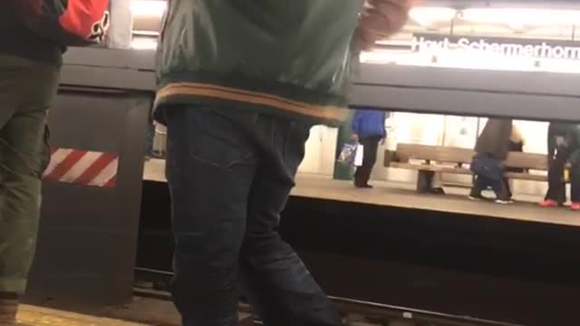 Man in green orange jacket dances on subway platform
