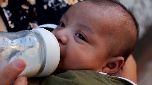 Person Carrying a Baby Feeding on the Milk Bottle