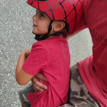 Little boy spiderman helmet skateboard dad down street