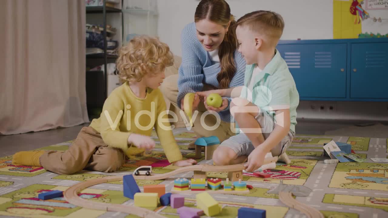 Children Playing With Cars And Pieces Of Wood Sitting On A Carpet In A Montessori School