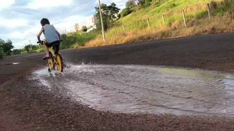 Boy Rides A Bike Through A Puddle