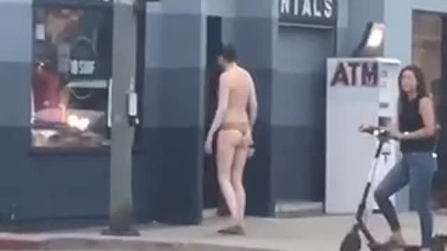 Guy in tiger print speedo shirtless standing in front of store