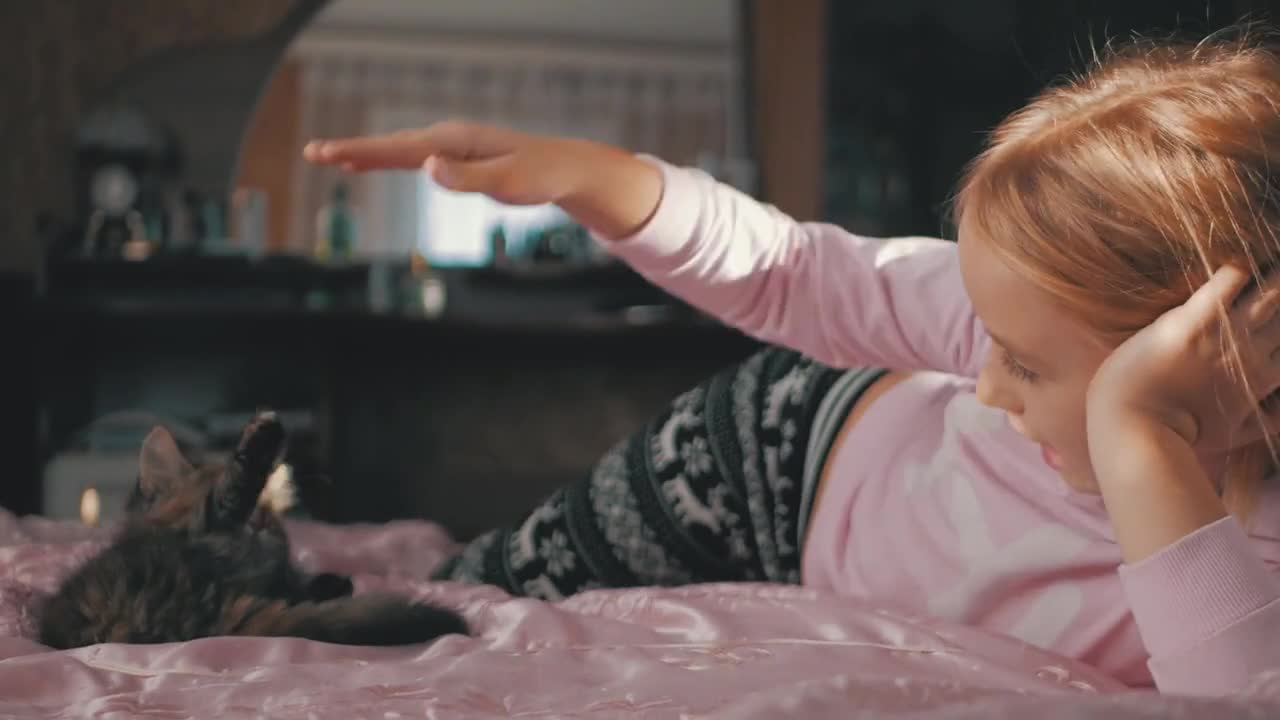 Little cute girl playing with kitten on bed at home