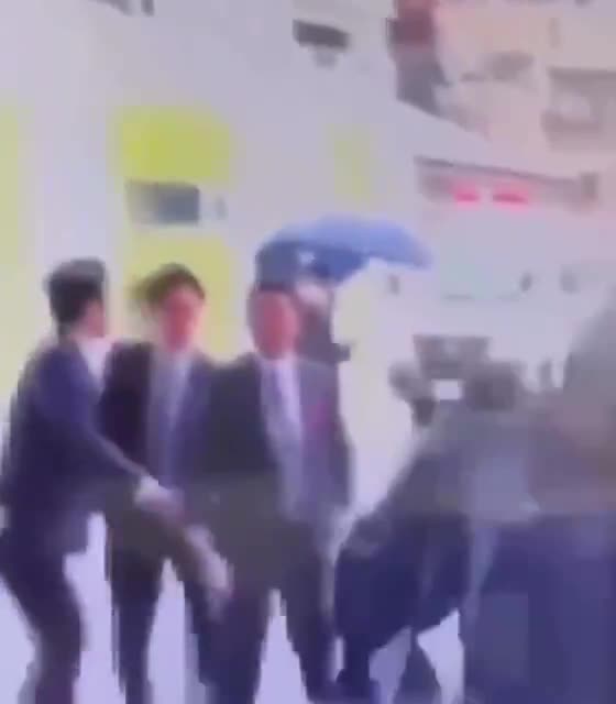 A bodyguard blocks an explosive, kicks it away, and quickly unfolds a shield while evacuating the Japanese Prime Minister