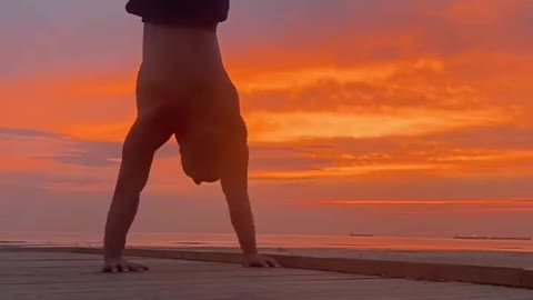 Guy Performs Upside Down Push-Ups And Pull-Ups While Hanging On Grill Wall During Sunset