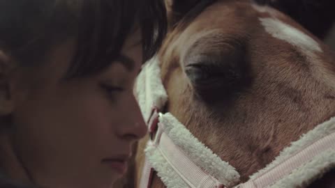 Young woman looks after her horse in the stall