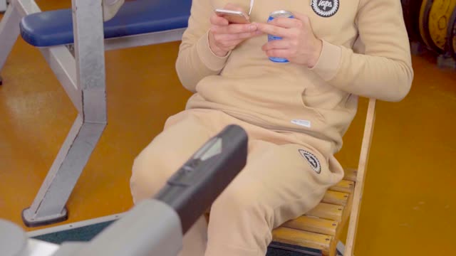 Man doing exercises on the treadmill while sitting on a chair, drinking a soda.