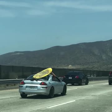 Yellow surf board on grey silver car roof
