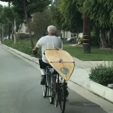 Old man white hair driving bike with surfboard in back