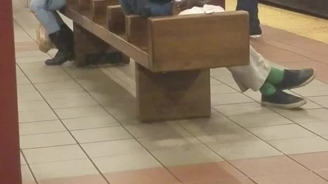 Homeless man smokes a cigarette and drinks out of water bottle on subway station bench