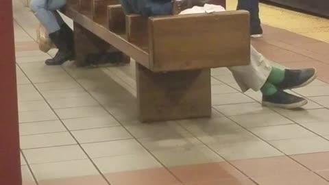 Homeless man smokes a cigarette and drinks out of water bottle on subway station bench 