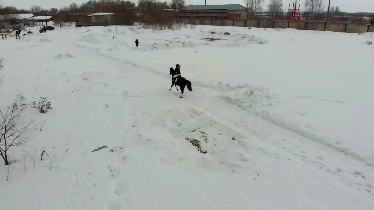 A young woman riding a horse on a snowy field in a village