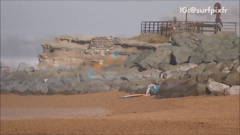 Surfer in blue wetsuit struggles to get out of water