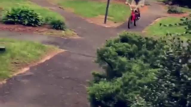 Grey sweater kid rides bike off sidewalk and through white fence