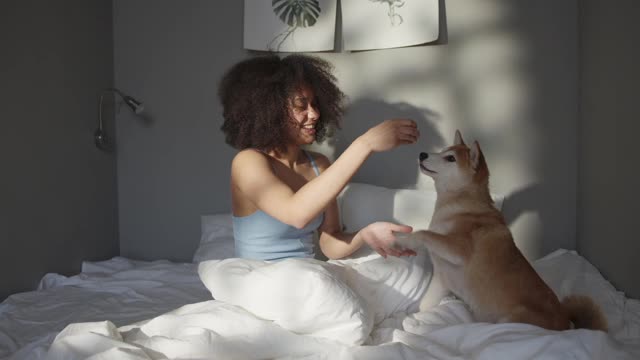 A Woman Teasing Her Pet Dog With Food While In Bed