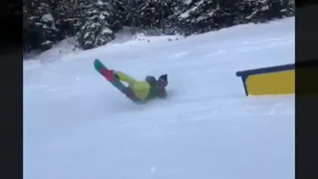 Green jacket yellow pants snowboarder lands on stomach