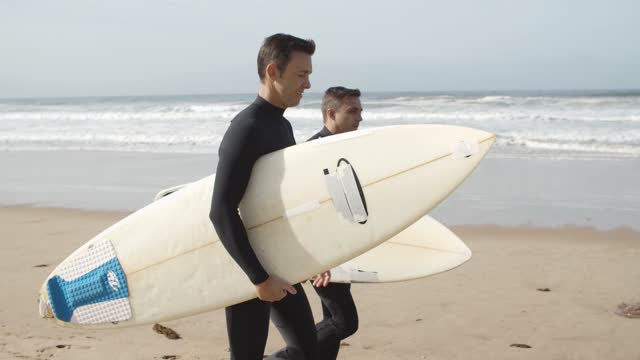 Surfers Walking In The Beach While Hold Surfboards