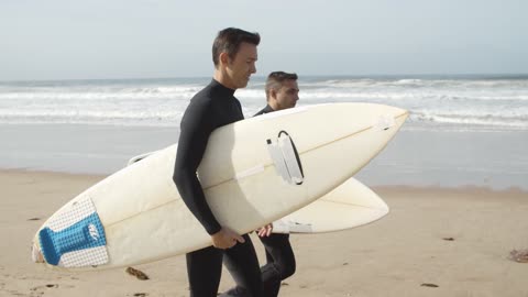 Surfers Walking In The Beach While Hold Surfboards