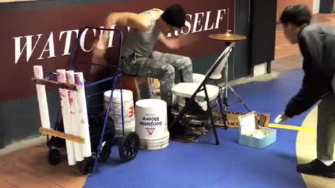 Guy plays the drums like crazy in subway station using containers, chairs, and wall