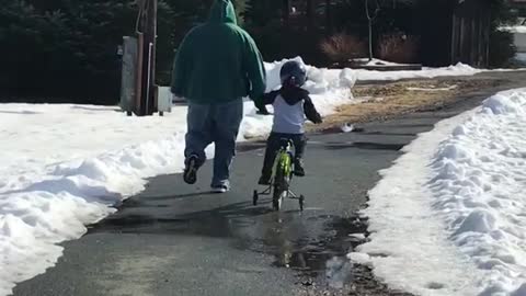 Man in green runs next to kid on bike and falls on her