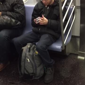Guy solving white rubik's cube and singing on subway train