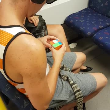 Guy in white orange shirt rubix cube on train