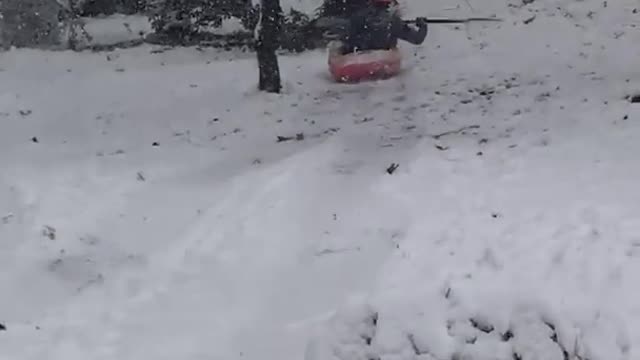 Red helmet kayak slides down snow hill into tree