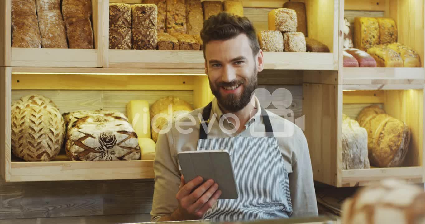 Young Man Bread Seller Scrolling And Taping On The Tablet Computer While Standing At The Counter In