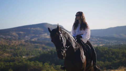 Portrait of gorgeous young woman sitting on brown horse in sunny mountains