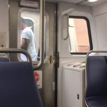 Guy standing outside between two subway carts trains