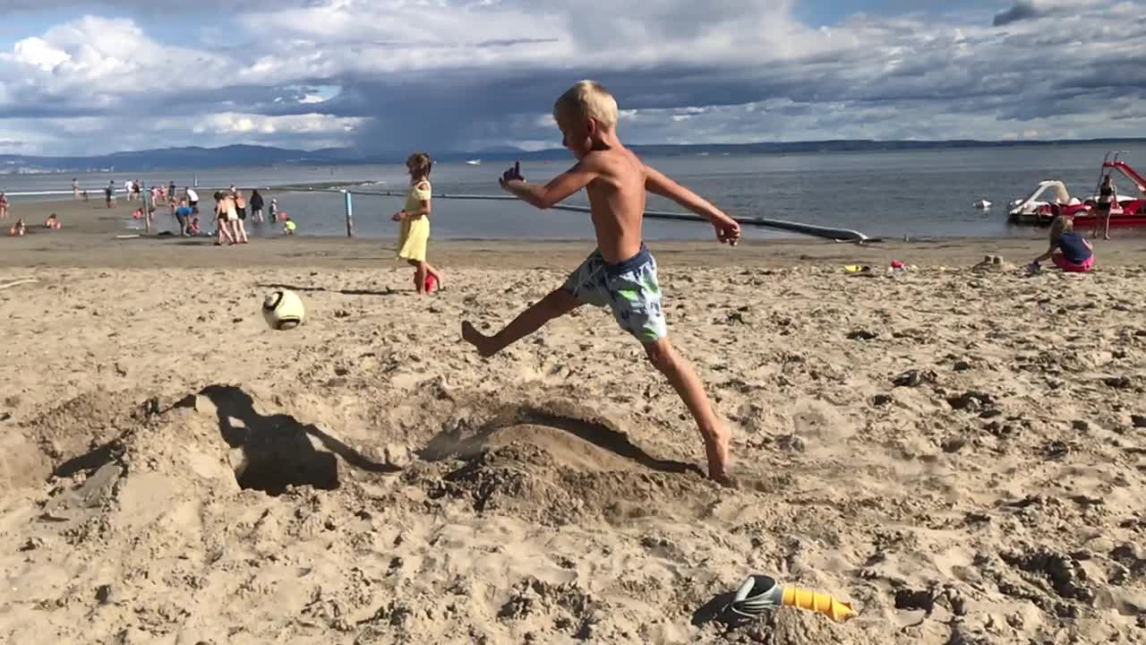 Blond boy in blue splits on sand